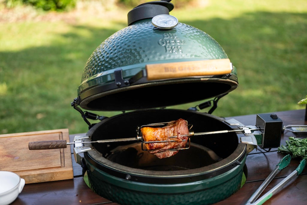 Green barbecue grill with rotisserie on a wooden table outdoors