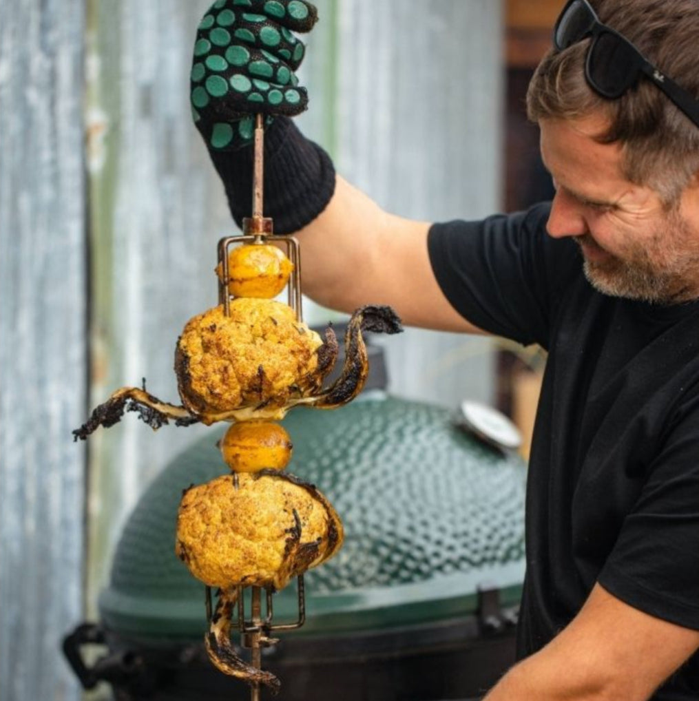 Person grilling cauliflower on a skewer with a Big Green Egg grill in the background