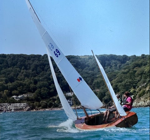 Sailing boat with a white sail on a clear day with green hills in the background