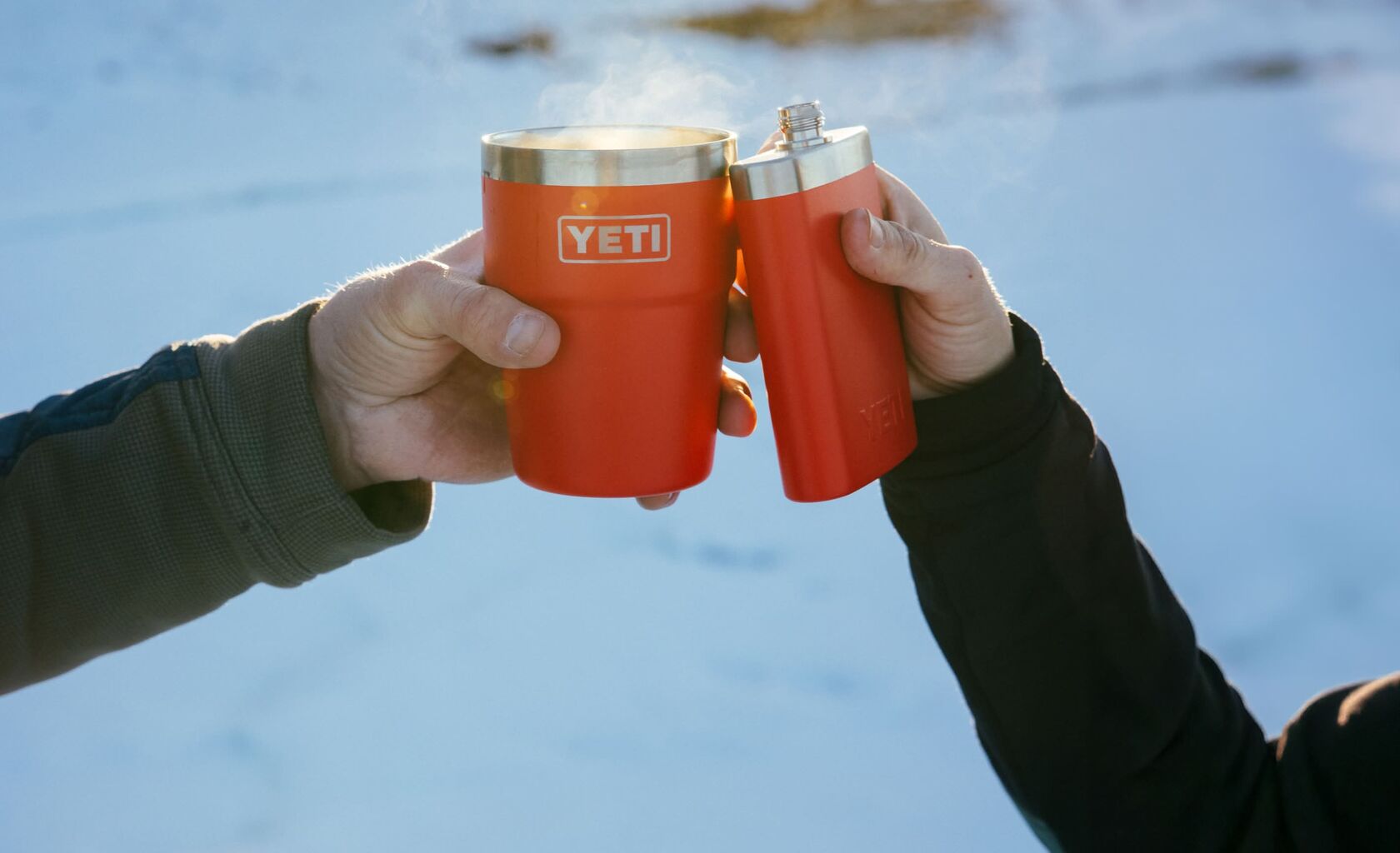 Two hands holding red YETI mugs with a snowy landscape in the background