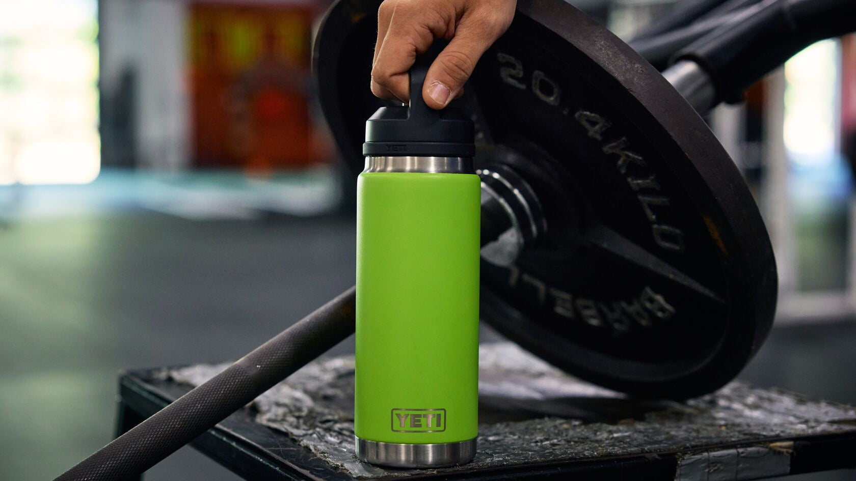 Green water bottle with black cap on a barbell in a gym setting