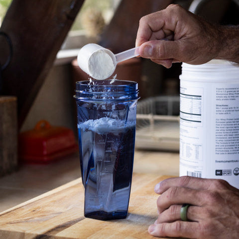 Person measuring protein powder into a blue Yeti cup on a wooden cutting board.