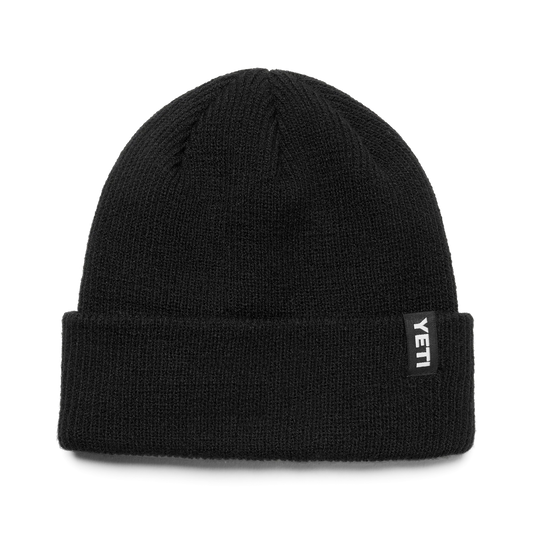 A black ribbed knit beanie hat with a folded cuff, featuring a small black rectangular brand patch on the side with the word 'YETI' in white.